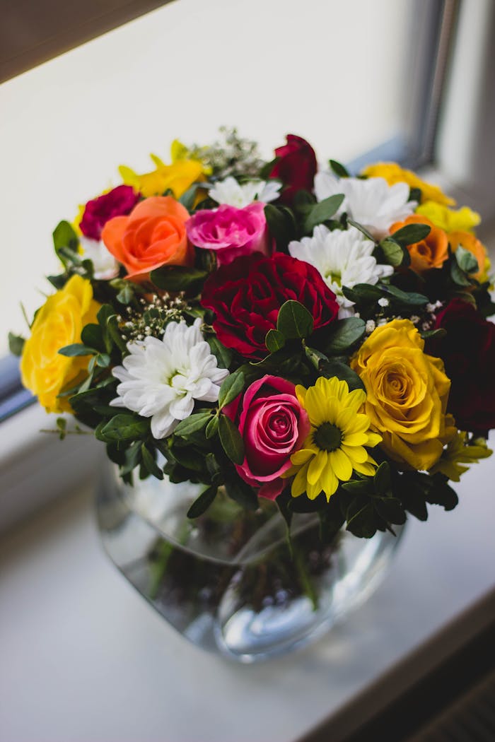 A colorful mix of roses and daisies in a glass vase on a windowsill, brightening the room.